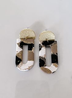 two pairs of black, white and gold earrings on top of a table with one earring in the shape of a rectangle