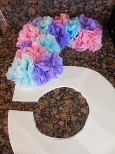 tissue paper flowers sitting on top of a white piece of paper in the shape of a letter