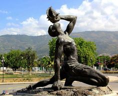 a statue of a woman sitting on top of a rock next to a street with mountains in the background