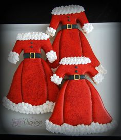 three decorated christmas cookies in the shape of santa's hats and gowns on a plate