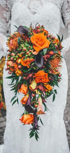 a bridal bouquet with orange flowers and greenery in the center is held by a bride