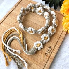 a wooden board topped with lots of white and yellow bracelets next to a flower