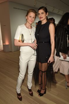 two women standing next to each other in front of a wooden floor with people looking on