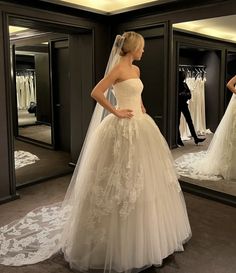 a woman standing in front of a mirror wearing a wedding dress