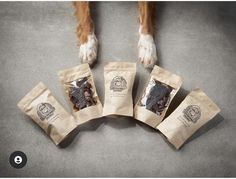 four bags of dog treats sitting on the floor next to a brown and white dog