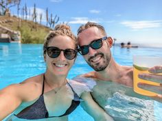 a man and woman taking a selfie in a swimming pool while holding up a drink