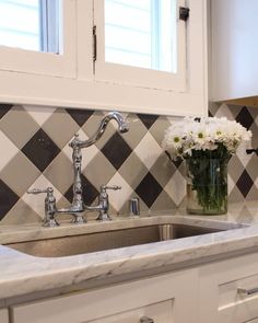 a white kitchen with black and white checkerboard backsplash, marble countertops and stainless steel sink