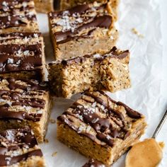 several pieces of cake with chocolate frosting and nuts on top next to a spoon