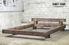 a wooden bed frame in front of a brick wall with posters on the wall behind it