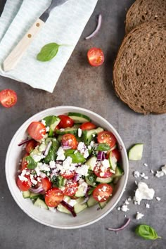 a salad with tomatoes, cucumbers and feta cheese in a white bowl