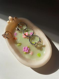 three rings are sitting on top of a soap dish with flowers in the bathtub