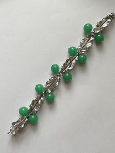 This is a stunning vintage silver tone metal and green Lucite bead cha-cha bracelet. The pieces signed Napier. It features a series of six dimensional leaf links with green beads in between the links. There are 10 beads This bracelet measures 8 inches long and is approximately 5/8 inches at the widest.  It appears to have never been worn. It is an excellent preowned vintage condition Retro Green Bracelet Jewelry, Green Metal Beaded Bracelets For Jewelry Making, Vintage Green Bracelets For Party, Green Metal Bracelets For Formal Occasions, Formal Green Metal Bracelets, Green Costume Jewelry Bracelets For Party, Vintage Green Beaded Bracelets, Vintage Green Round Bead Bracelets, Vintage Green Round Beads Bracelet