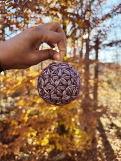 a hand holding an ornament in front of a tree filled with autumn leaves