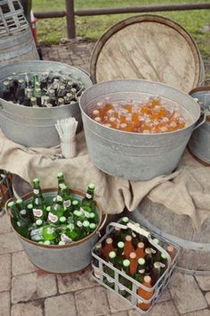 several buckets filled with different types of bottles on top of a brick floor next to barrels