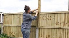 a woman standing next to a wooden fence with her hands on the top of it