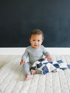 a baby sitting on top of a bed with a blanket