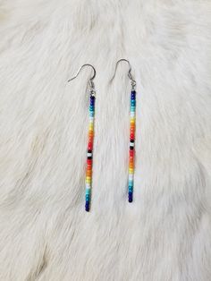 a pair of earrings with multicolored beads hanging from them on a white fur surface