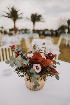 an arrangement of flowers and greenery in a vase on top of a white table