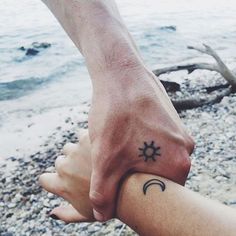 two people holding hands with the sun and moon tattooed on their wrists in front of water