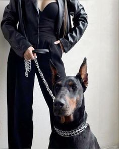 a woman in black is standing next to a dog wearing a chain around her neck