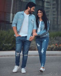 a man and woman holding hands walking down the street