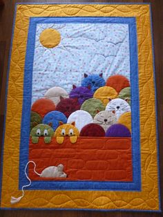 a quilted wall hanging with cats and balls on it's side, in front of a wooden floor