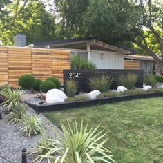 a house with landscaping in front of it and trees on the other side of the fence