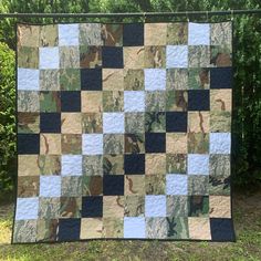 a quilt is hanging on a clothes line in front of some trees and bushes,