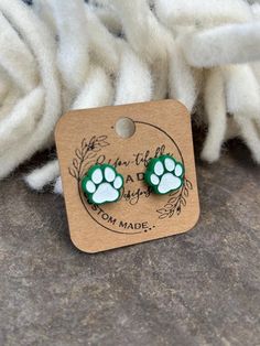 a pair of green and white paw print earrings on top of a pile of wool