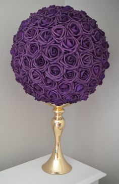 a gold vase with purple flowers on it sitting on a white shelf next to a wall