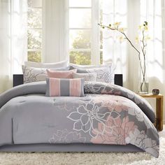 a bed with grey and pink comforters in front of a window on a white rug