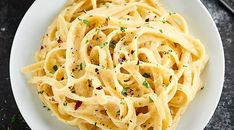 a white plate filled with pasta and parsley on top of a black tablecloth