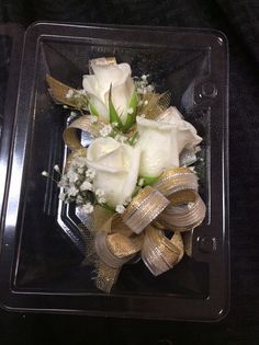 white roses and baby's breath tied together in a clear box with gold ribbon