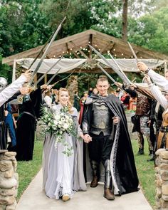 a man and woman dressed up in medieval costumes are walking down the aisle with swords