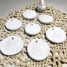 six white round buttons sitting on top of a doily next to a small bird