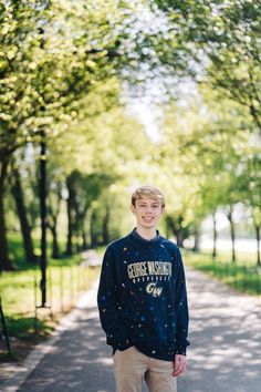 a young man standing on the side of a road wearing a sweatshirt and khaki pants