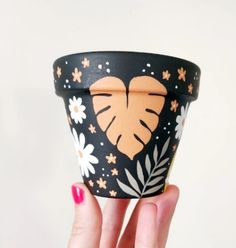 a hand holding up a black and white cup with an orange heart painted on it