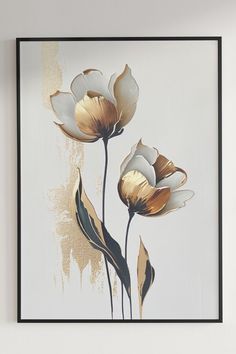 two white and gold flowers in a black frame hanging on the wall next to a vase