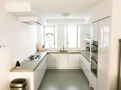 a white kitchen with stainless steel appliances and counter tops, along with a trash can on the floor