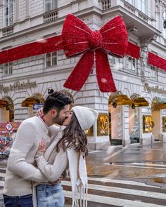 a man and woman kissing in front of a large red bow