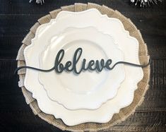 a white plate with the word believe on it sitting on a wooden table next to christmas decorations