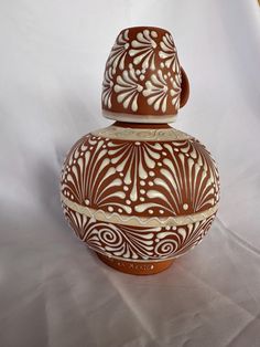 a brown and white vase sitting on top of a white tablecloth covered floor next to a wall