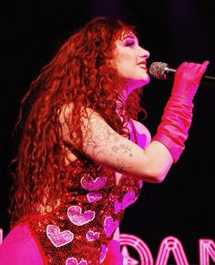 a woman with long red hair is holding a microphone in her right hand and singing into the microphone