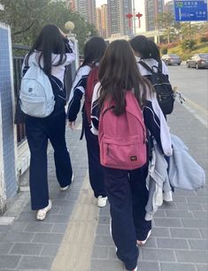 three girls walking down the sidewalk with backpacks on their back and one girl in blue pants