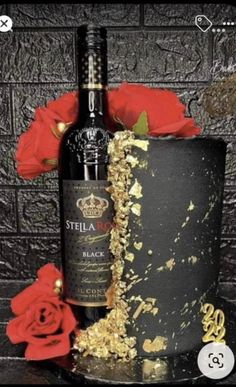 a black cake with gold sprinkles next to a bottle of wine and red roses