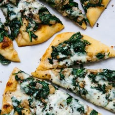 several slices of pizza with spinach and cheese on them sitting on a white surface