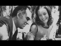 a man and woman sitting at a table with food in front of them, looking at each other