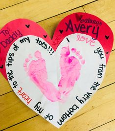 two paper hearts with handprints on them sitting on a wooden floor next to each other