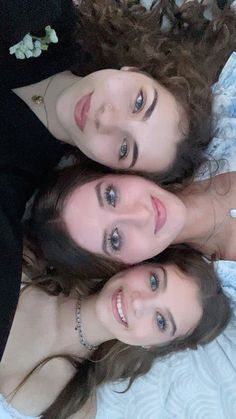 three young women laying on top of a bed next to each other