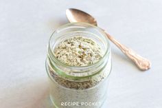 a jar filled with food next to a spoon on top of a white tablecloth